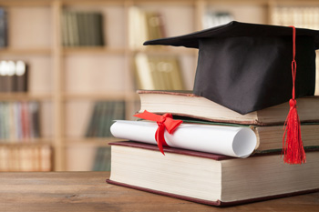stack of textbooks with a scroll and graduation cap sitting on top